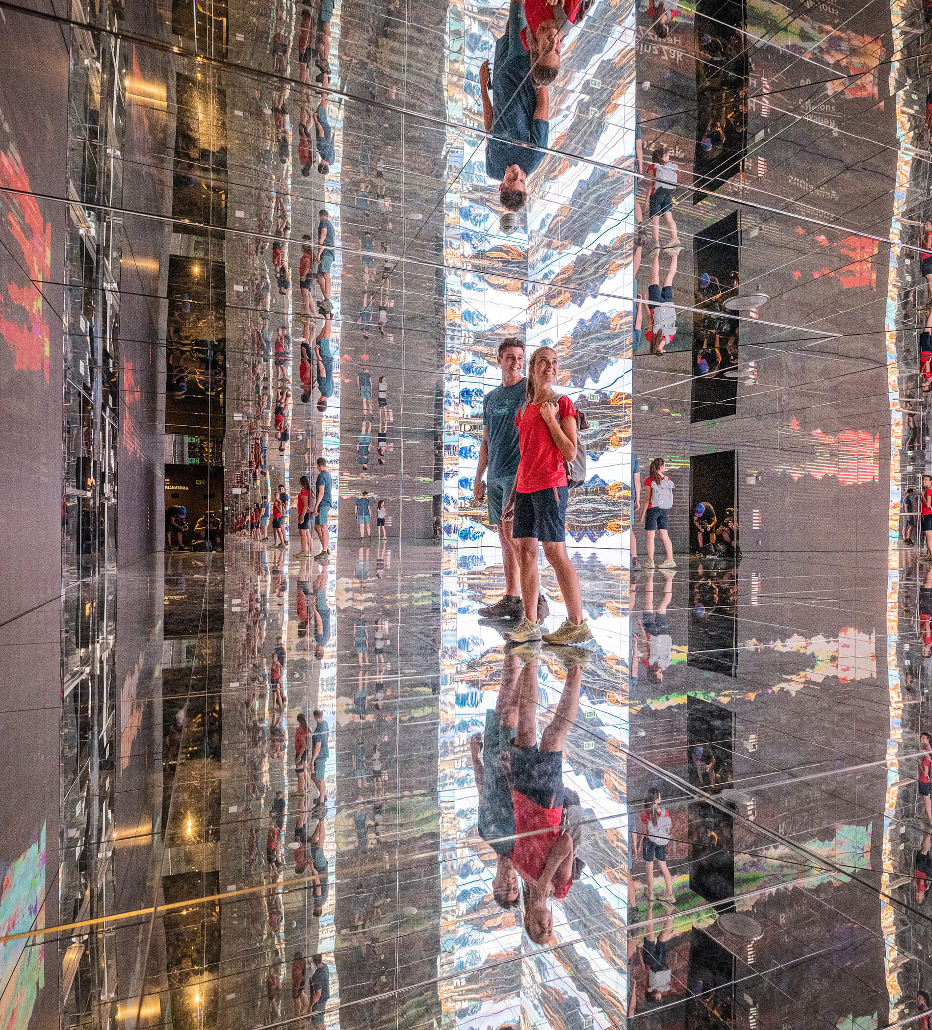 Two people stand in a mirrored room, creating multiple reflections on the walls, floor, and ceiling. - Ampark