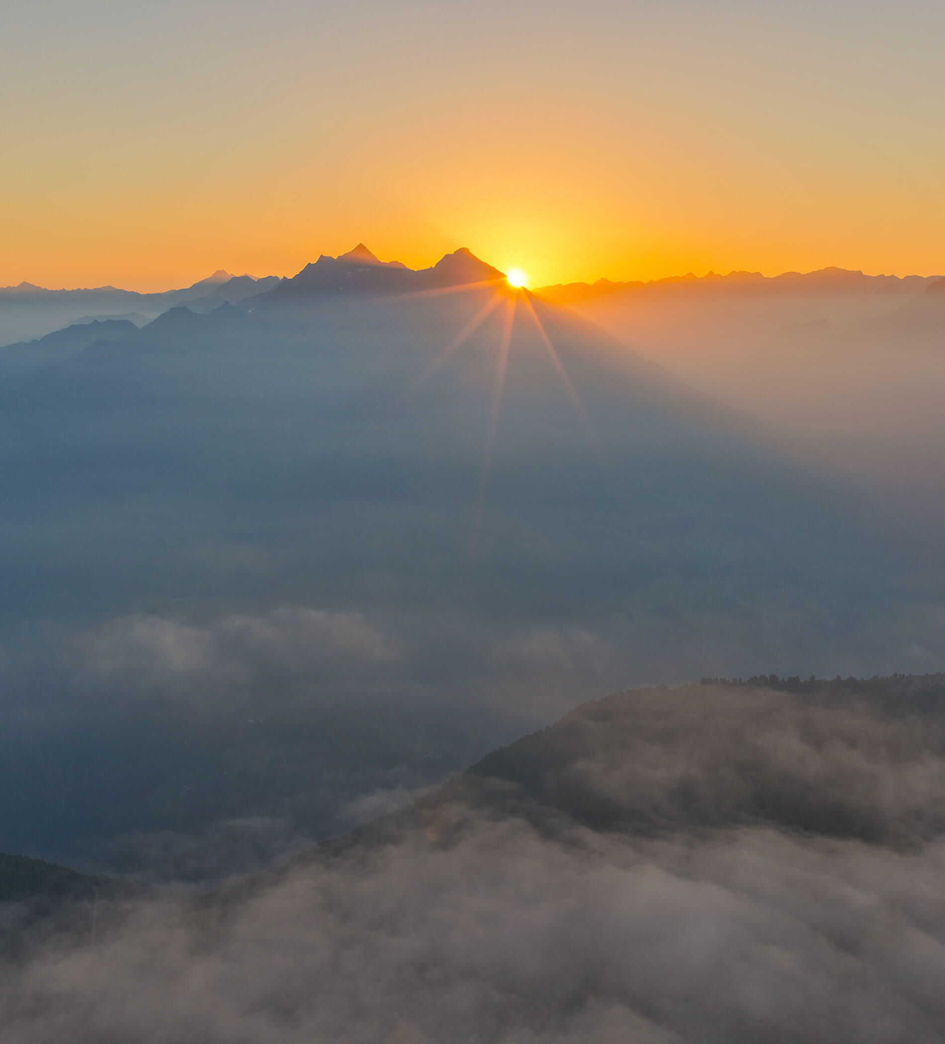 Sunrise over misty mountains with sunlight shining above the peaks and clouds below. - Ampark