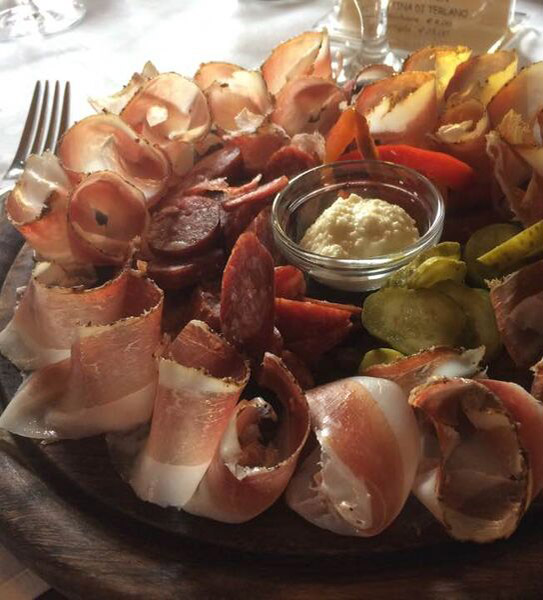 Eine Wurst- und Aufschnittplatte mit Wurstwaren, in Scheiben geschnittenen Gewürzgurken, Paprika und einer kleinen Schale mit cremigem Dip. - Ampark