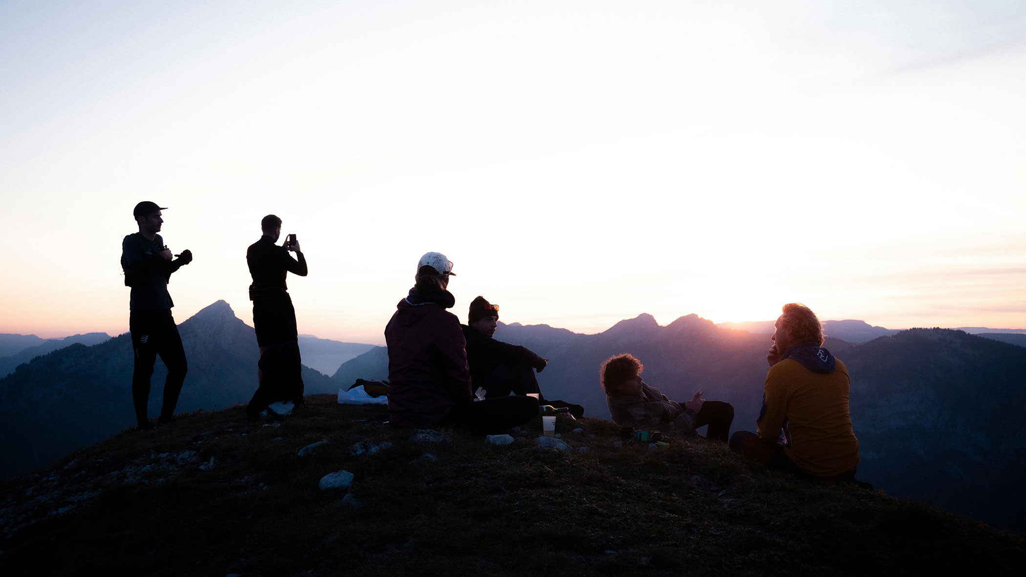 Six people sit and stand on a hilltop at sunset, with mountains in the background. - Ampark
